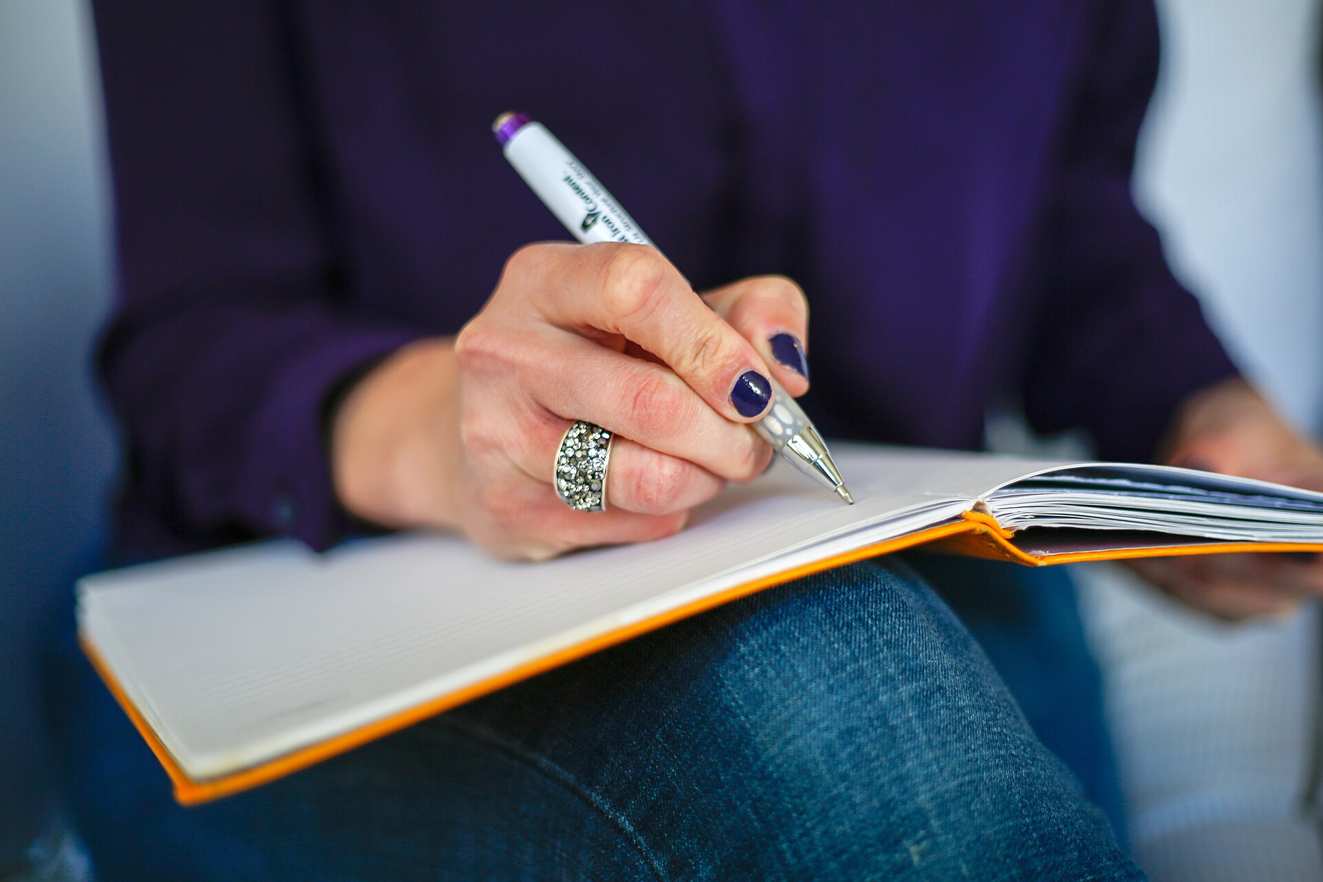 A hand writing in an orange-covered notebook